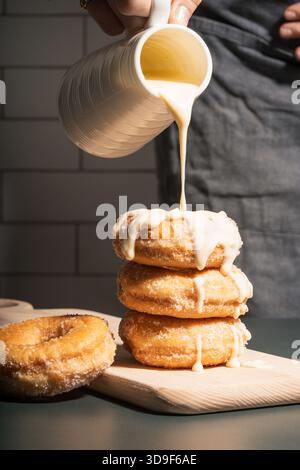 white chocolate being poured over stacked sugar donuts Stock Photo