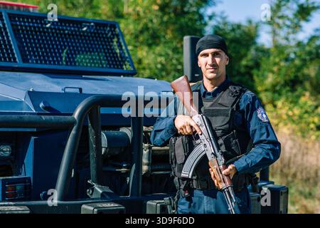 A Kosovo police officer stands guard with an automatic rifle next to an armored vehicle at the Banjska border area during heightened security measures Stock Photo