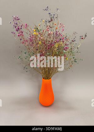 Orange Art object flower vase printed on 3D printer from melted orange plastic with colorful flowers. progressive technology 3D printing recycling Stock Photo