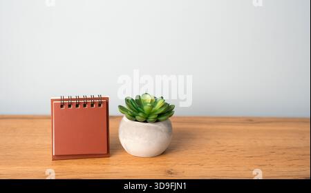 Blank empty notepad standing next to a succulent on a wooden desk, creating a minimalist workspace scene, inspiring creativity, planning, and organiza Stock Photo