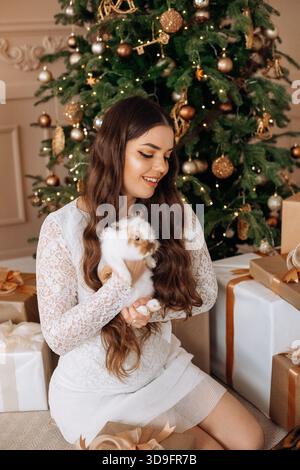 A joyful woman is sitting on the floor, cradling an adorable rabbit while smiling. Stock Photo