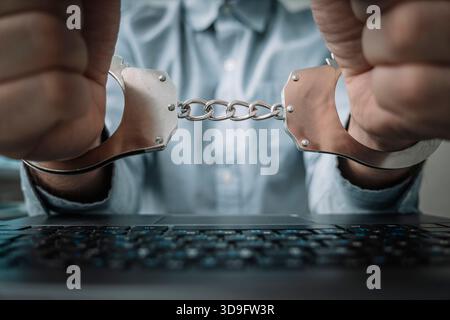 Hacker using laptop. Detail of business person hand tied with handcuffs to workplace, Hacker hand in handcuffs with laptop computer- internet cyber cr Stock Photo