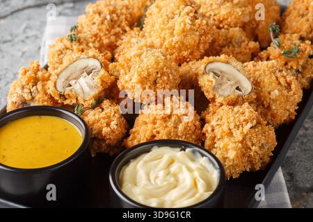 White button mushroom breaded with seasoned panko bread crumbs and deep-fried to golden perfection close-up in a plate on the table. Horizontal Stock Photo