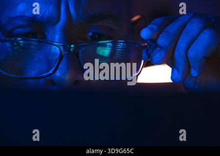 Person removing glasses while looking at data illuminated by blue screen light Stock Photo