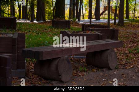 Simple wooden bench made from logs stands in a quiet forest park covered in fallen leaves, evoking a rustic and peaceful autumn atmosphere Stock Photo