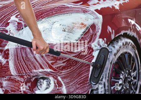 Red car washed in self serve carwash detail on brush moving over front hood above wheels, leaving strokes in white soap Stock Photo