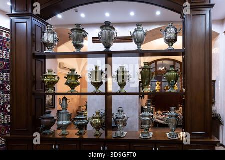 Elegant collection of antique brass and silver samovars on wooden shelves, celebrating rich Eurasian tea culture and heritage. Stock Photo