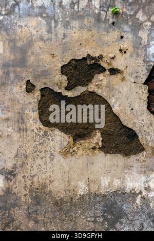A high-resolution, vertical texture featuring a large, irregularly shaped hole or void in faded, light brown stucco/concrete, revealing the darker, co Stock Photo