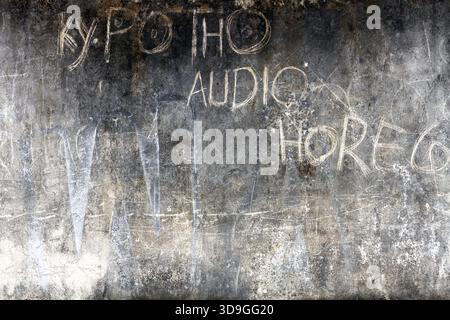 Dark, moody, horizontal grunge background of a textured concrete wall with faded, hand-scrawled chalk or scratched graffiti. The surface is heavily wa Stock Photo