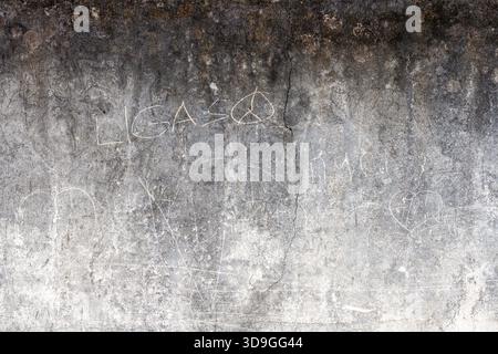High-contrast, horizontal, dark-to-light gradient on a grungy concrete wall heavily scratched with a peace sign and faded text. Features deep water-da Stock Photo