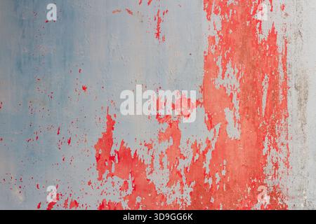 A vibrant, horizontal abstract texture showcasing dynamic vertical splashes of bright red paint aggressively peeling away from a pale blue-grey concre Stock Photo