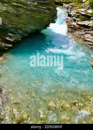 A vivid turquoise mountain stream flows powerfully through dark slate rock formations near the Mattmark Reservoir above Saas-Fee, Valais, Switzerland Stock Photo