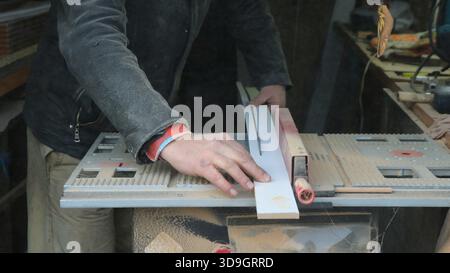 A carpenter saws a long narrow board on a circular saw in an open-plan workshop, working with wood on a machine tool, processing and preparing Stock Photo