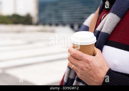 Man standing on urban plaza holding takeaway coffee cup while wearing striped sweater, copy space Stock Photo