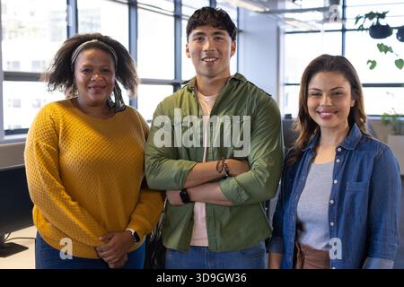 Diverse coworkers posing in open office with windows using computers and desk chairs with plants Stock Photo