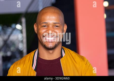 Smiling adult African American man standing in lobby wearing mustard yellow jacket, maroon sweater Stock Photo