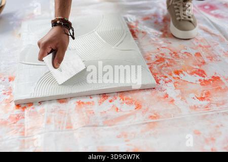 Indian male using notched trowel applying adhesive mortar onto tile on sheet during renovation Stock Photo
