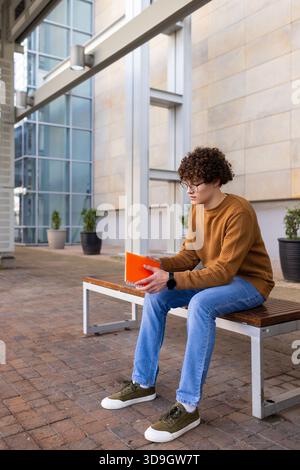 Man sitting on bench in courtyard with potted plants holding orange spiral notebook, copy space Stock Photo