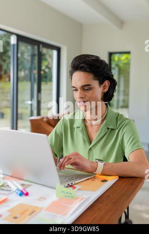 Man typing on laptop and sorting papers at wooden table in modern room with sticky notes Stock Photo