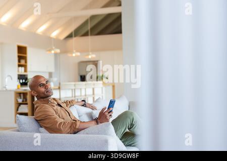 African American man reclining on sofa in modern living room while gazing at smartphone, copy space Stock Photo