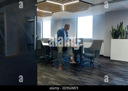 Silver laptop sitting on conference table in office beside potted snake plants under LED lighting Stock Photo