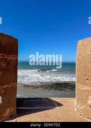 Atlantic waves framed between old Essaouira ramparts, view from the stone fortification, vivid blue sky, sunny day and calm, peaceful ocean Stock Photo