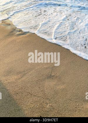 Gentle wave washing the smooth sandy beach, soft foam patterns on wet sand background, close-up view from above, copy space, summer vacation card temp Stock Photo