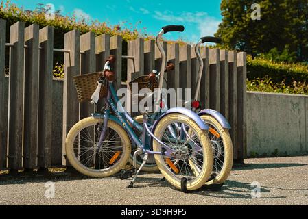 Two kids bicycles parked on a sunny day under a clear blue sky but patchy clouds, near Roskilde Marina Stock Photo