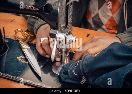 Closeup of hands sewing fabric with a vintage sewing machine and scissors on a wooden table Stock Photo
