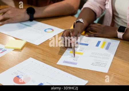 African American coworkers reviewing data on wood table woman wearing pink blazer holding metal pen Stock Photo