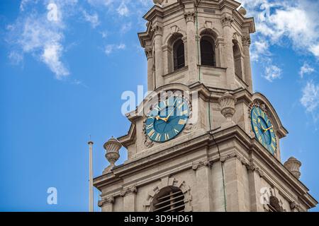 The bell tower of Saint Martin in the Fields shows its two clocks against a bright blue sky. The tower features stone details and is in London. Stock Photo