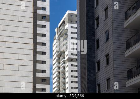 Framed view of newly built residential high rise with stacked glass balconies and stone cladding under clear blue sky. Contemporary urban housing and real estate development Stock Photo