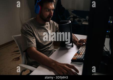 Gamer wearing colorful headphones playing computer video games at desktop setup, streaming online content and participating in esports competition Stock Photo