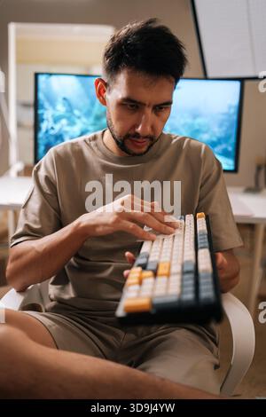 Vertical portrait of focused technician cleaning mechanical keyboard, wiping dust and germs from input device keys. Maintaining hygiene and sanitation Stock Photo