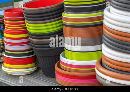 Close view of stacked plastic flower pots and buckets in assorted colors for gardening and retail sale. Bright round containers with ribbed rims and saucers for home and outdoor planting Stock Photo