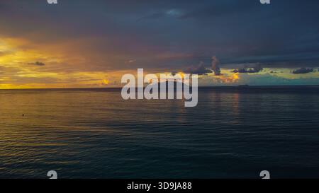 Ocean Horizon with Hazy Island Mass: Golden Sun Breaking Through Dark Clouds Stock Photo