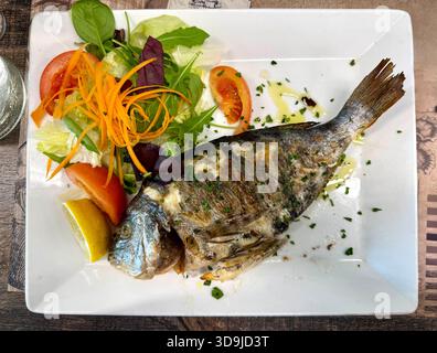 portion of grilled sea bream fish and vegetables on white plate on restaurant table, top view Stock Photo
