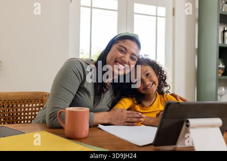 Indian mother and daughter laughing and using tablet stand and pencil at home dining area Stock Photo