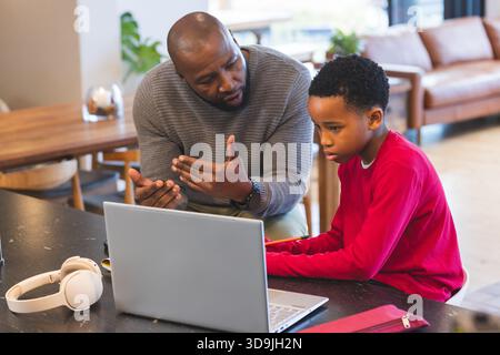 African American father and son working in living room using laptop with headphones and pencil case Stock Photo