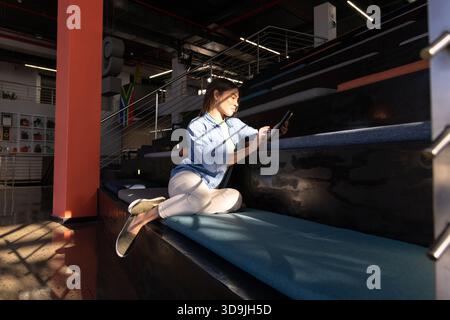 Adult Indian woman using digital tablet with stylus and sitting on tiered bench in coworking lounge Stock Photo