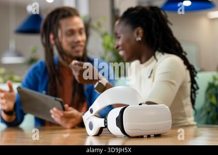 African American coworkers talking around VR headset in office, woman wearing smartwatch Stock Photo