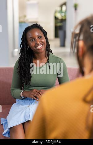 African American colleagues chatting on muted pink sofa in office lounge, showing gold necklace Stock Photo
