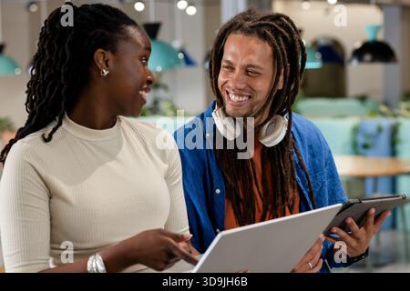 African American students collaborating on laptop and tablet with headphones and stylus in lounge Stock Photo