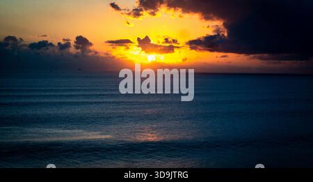 Dramatic ocean sunset with vibrant orange and dark clouds. Stock Photo