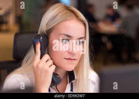 Female security officer communicating via phone while monitoring activity inside a modern surveillance control room. Stock Photo