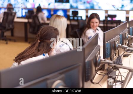 Group of female security officers working and communicating inside a modern surveillance control room. Stock Photo