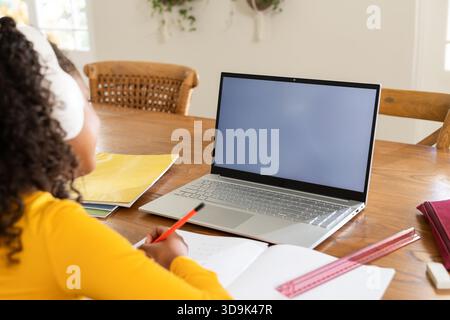 Silver laptop sitting on wooden study table with notebook and red pencil resting by sunlit window Stock Photo
