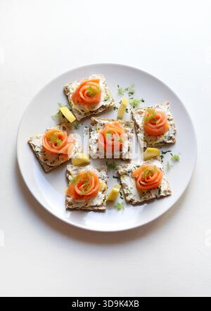 Smoked salmon and cream cheese canapés on wholemeal crackers, garnished with dill and lemon, on a white background. Christmas and holiday season. Stock Photo