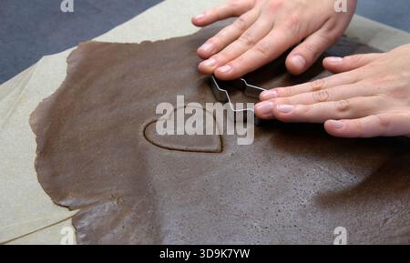 Metal Christmas-tree cutter resting on rolled brown dough beside a heart-shaped outline on parchment. Stock Photo