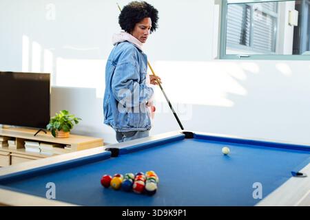 African American man holding pool cue aiming balls on blue-felt table in game room, copy space Stock Photo